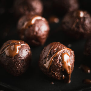 Close-up of chocolate date balls with a drizzle of chocolate sauce on a dark surface.