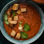 Bowl of creamy tomato soup with fresh basil and croutons on top.
