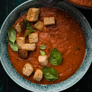 Bowl of creamy tomato soup with fresh basil and croutons on top.