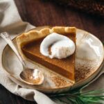 A slice of vegan pumpkin pie topped with whipped cream and a sprinkling of cinnamon.