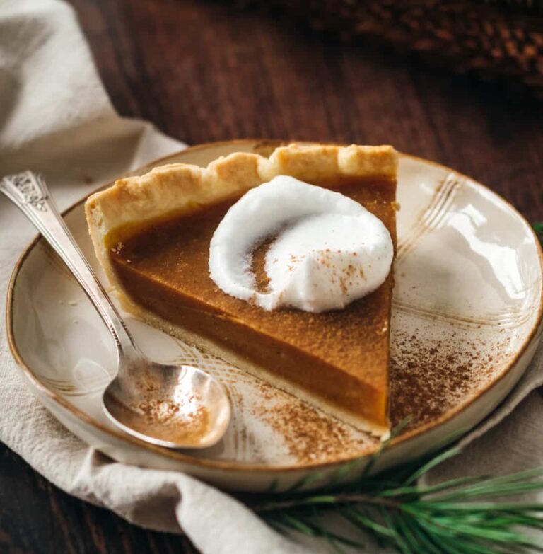A slice of vegan pumpkin pie topped with whipped cream and a sprinkling of cinnamon.