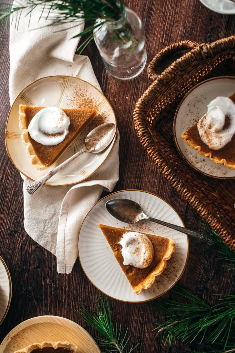 Three plates of vegan pumpkin pie with whipped cream are placed on a wooden table.