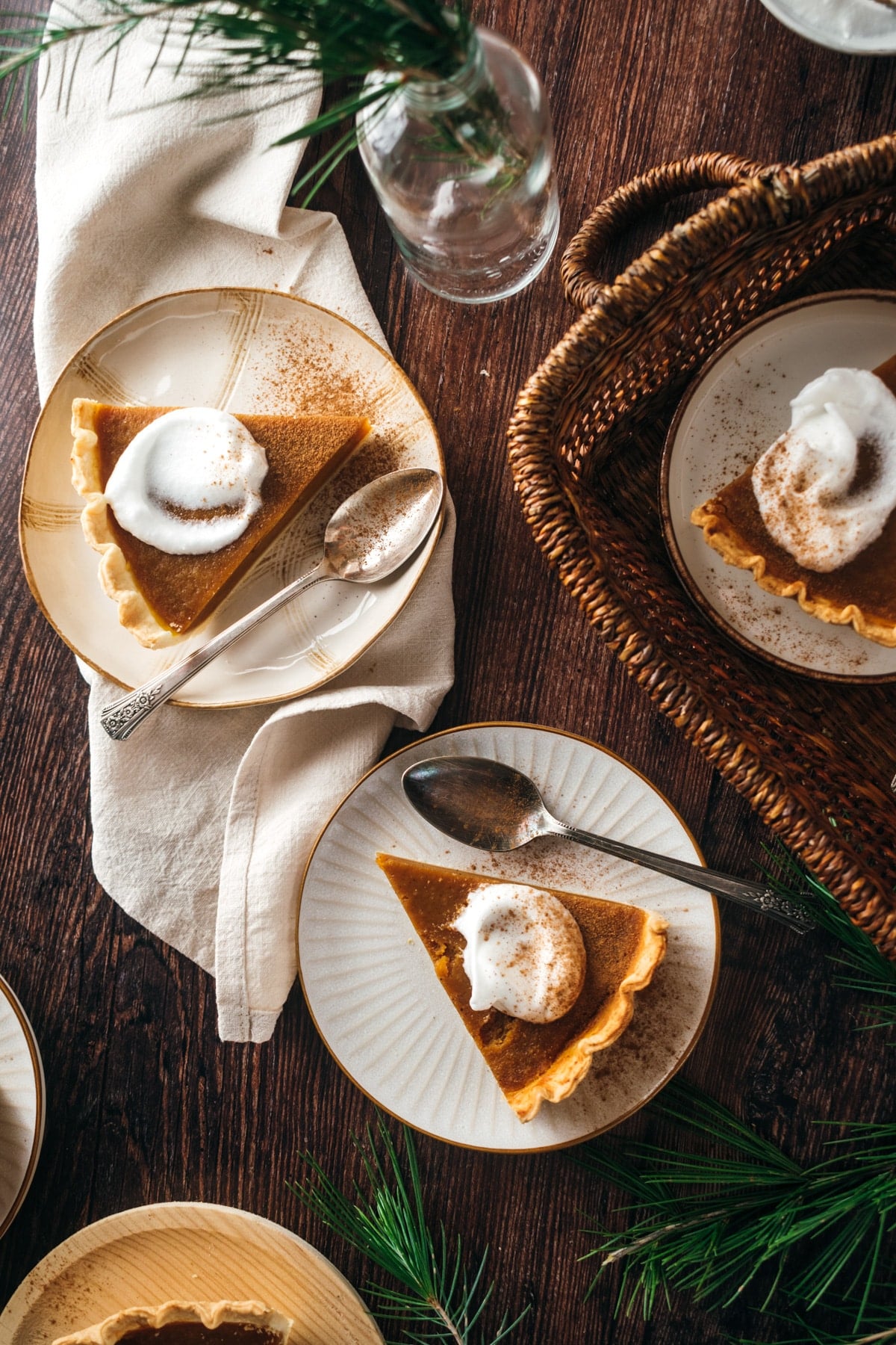 Three plates of vegan pumpkin pie with whipped cream are placed on a wooden table.