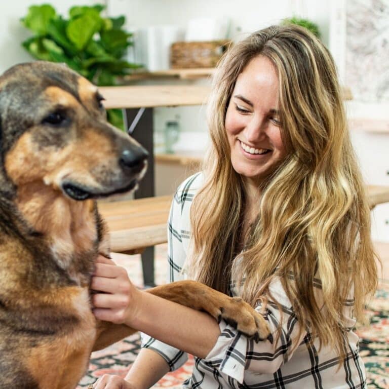 Smiling woman sitting on the floor petting a large dog.