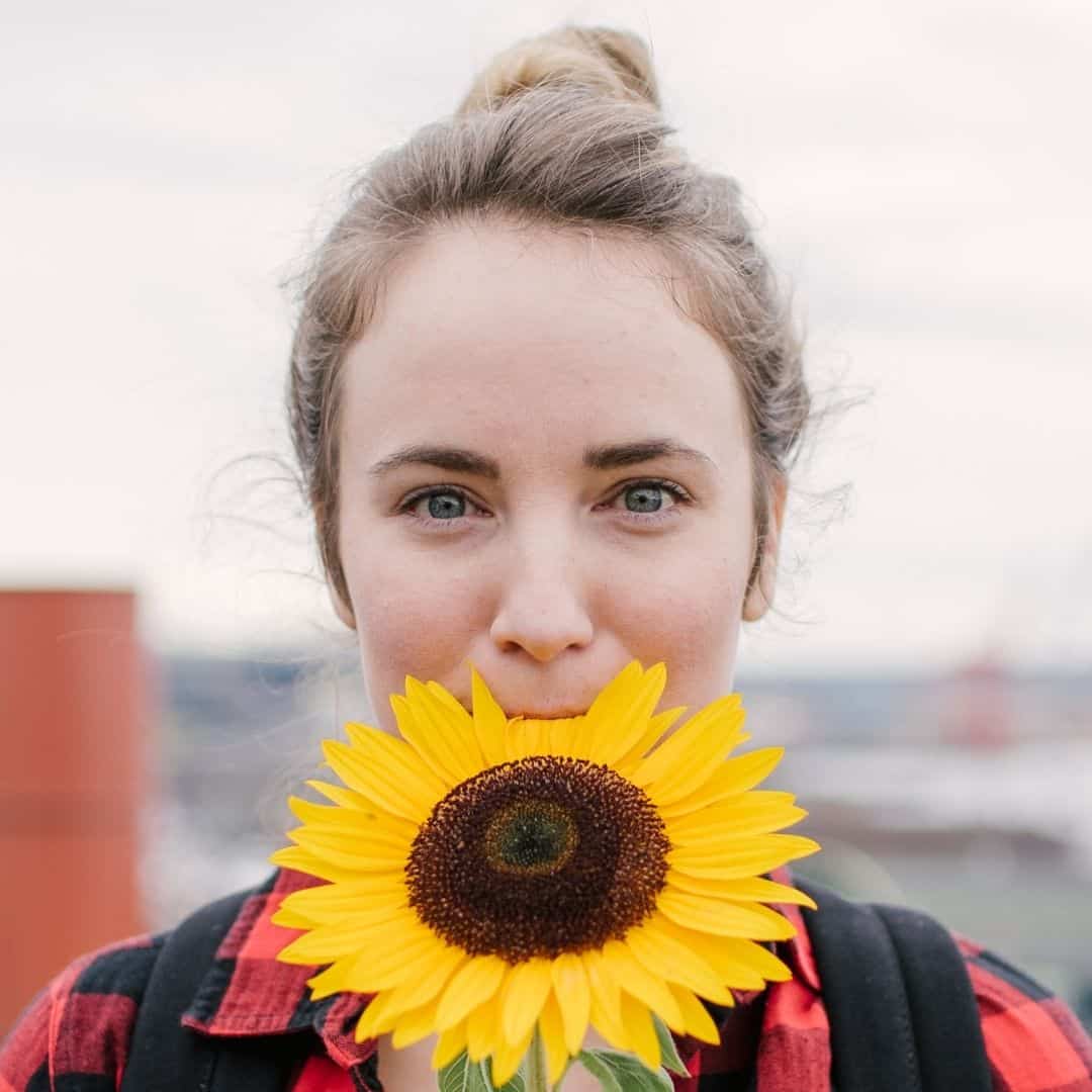 Woman wearing plaid with a sunflower by her face.