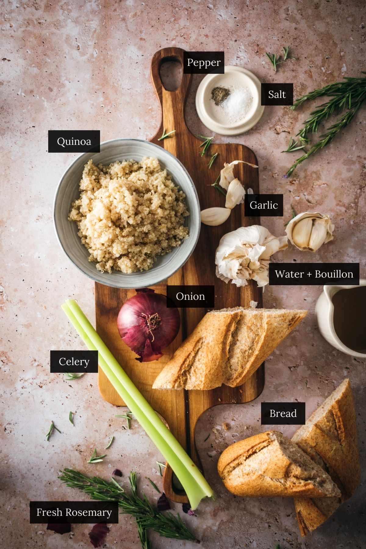 Top-down view of cooking ingredients for vegan stuffing: quinoa, garlic, salt, pepper, water with bouillon, onion, celery, fresh rosemary, and bread laid out on a wooden board.