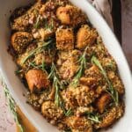 A dish of vegan stuffing made with quinoa, bread cubes, and fresh rosemary is elegantly presented in an oval white serving dish.