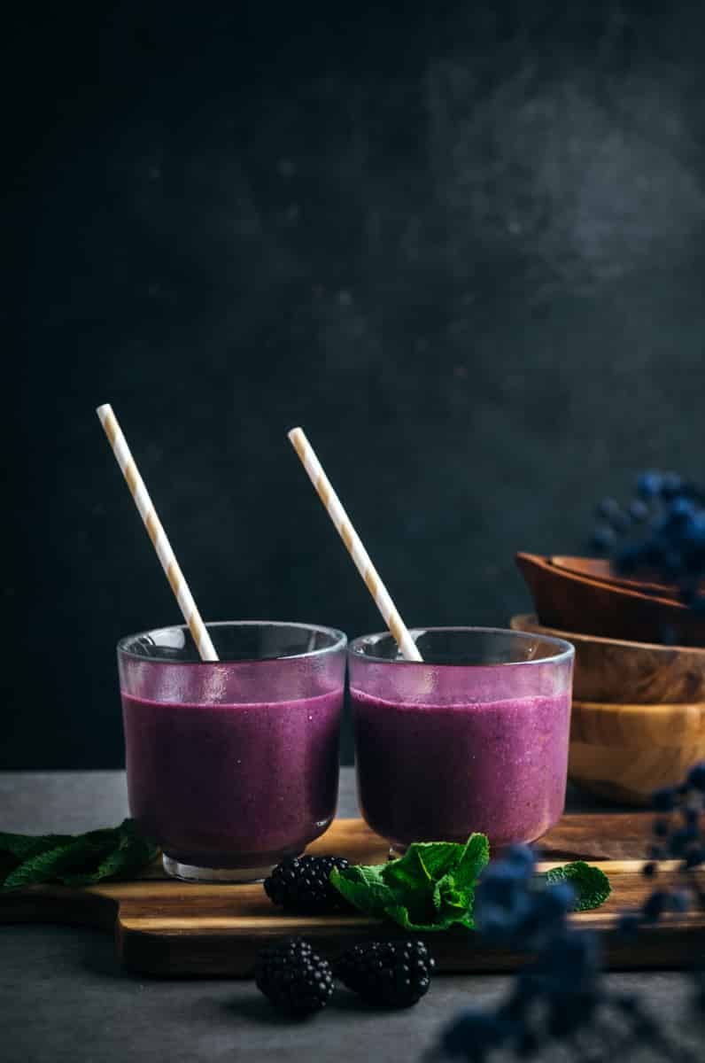 Two glasses of deep purple blackberry smoothie with paper straws.