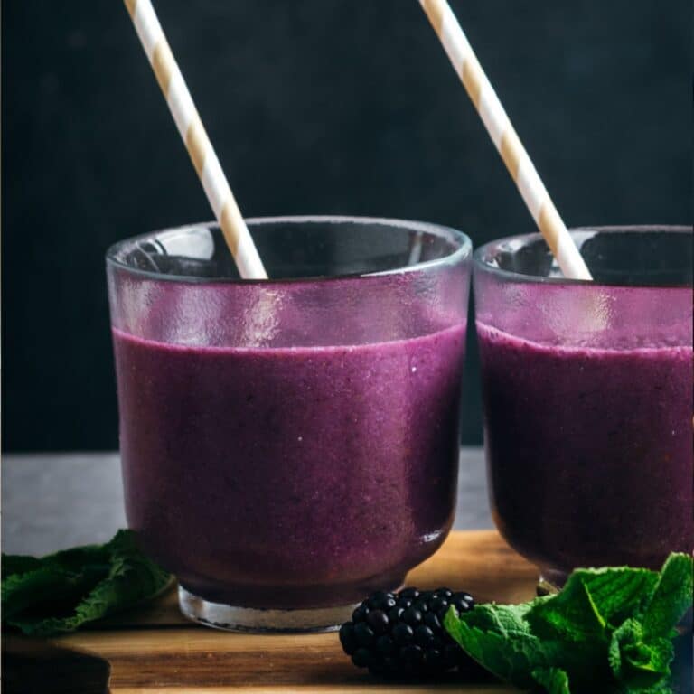 Deep purple smoothie in a glass with a paper straw.