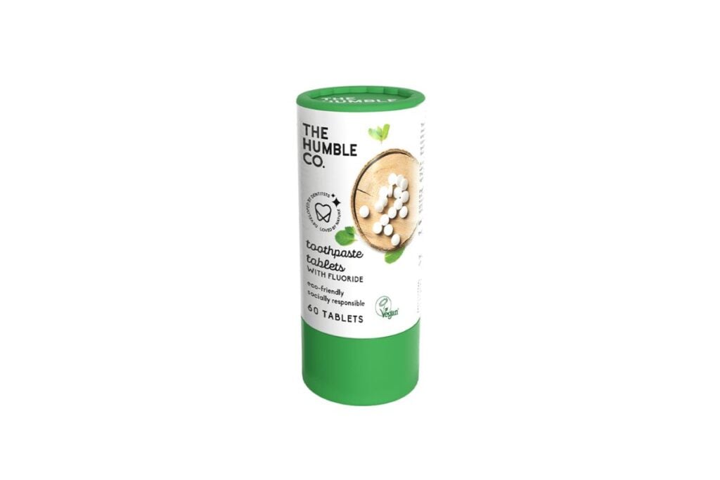 Cardboard tube with a green lid filled with zero-waste toothpaste tablets.