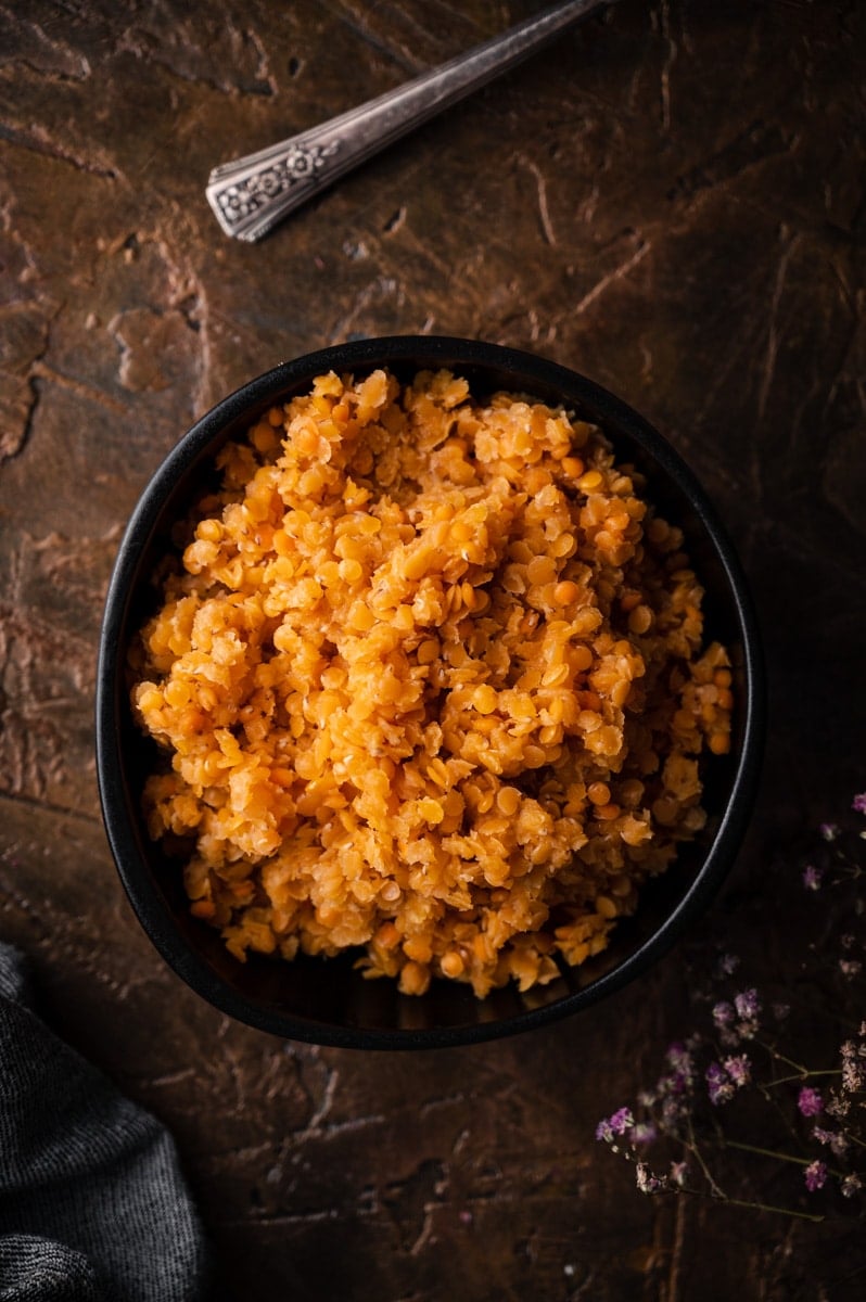 Top down view of cooked red lentils in a black bowl.