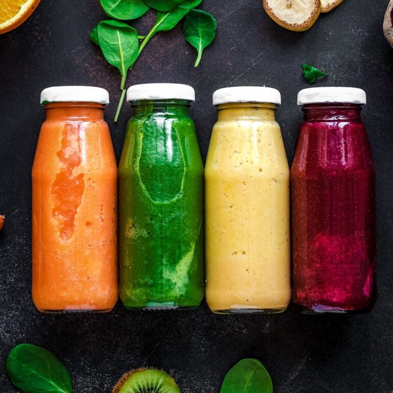Four glass bottles filled with different veggie smoothies.