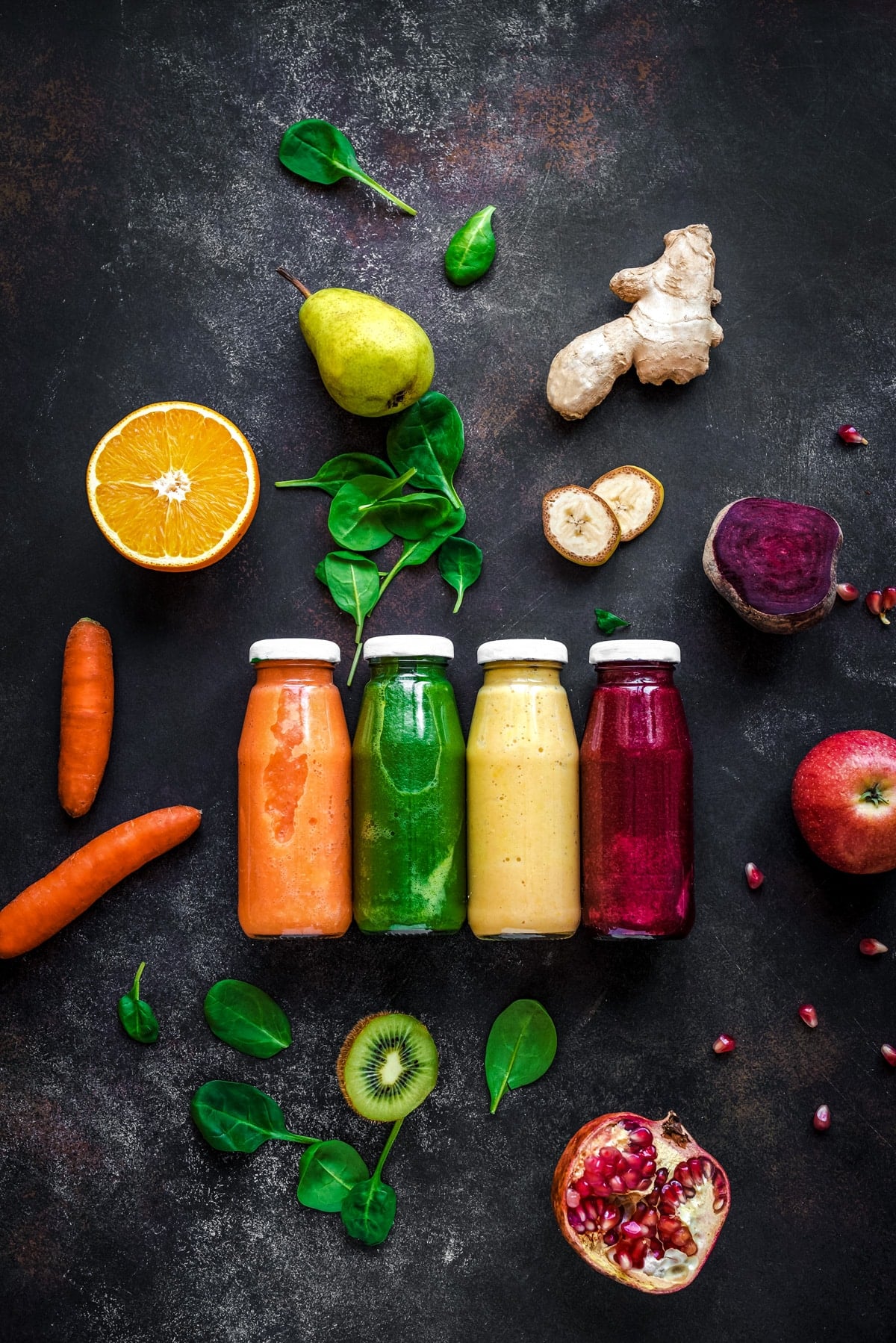 Bright orange, green, yellow, and dark pink vegetable smoothies with fresh fruit and veggies around. 