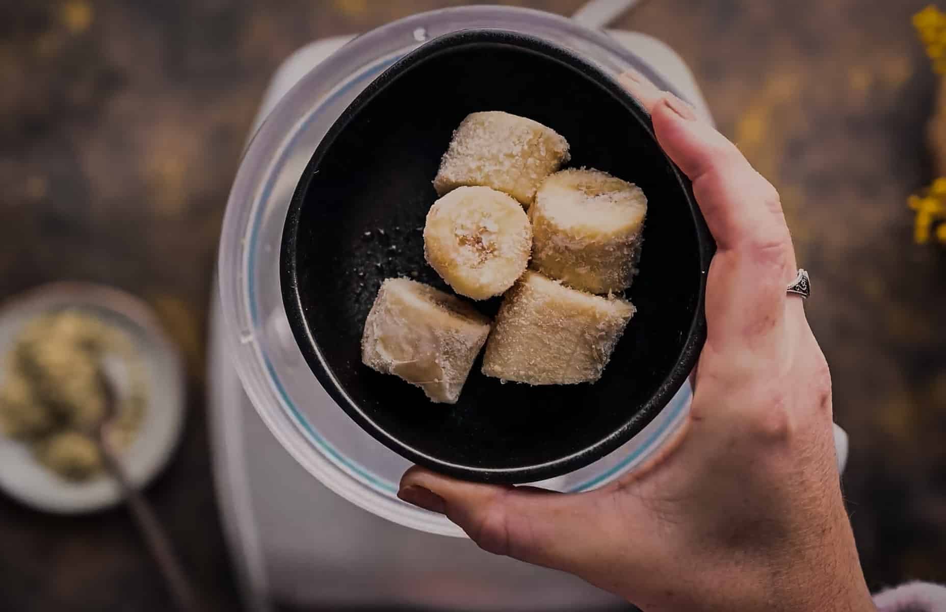 Hand holding a black bowl with several pieces of frozen banana inside.