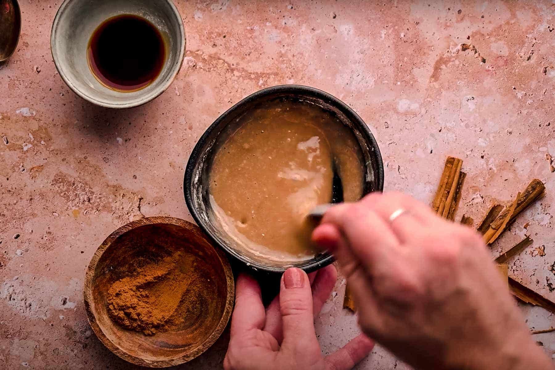 A person stirs a brown cinnamon glaze in a small bowl.