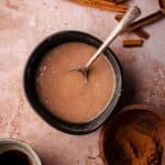 A creamy glaze in a black bowl with a silver spoon on a textured surface.