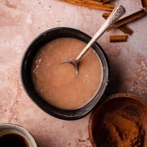 A creamy glaze in a black bowl with a silver spoon on a textured surface.