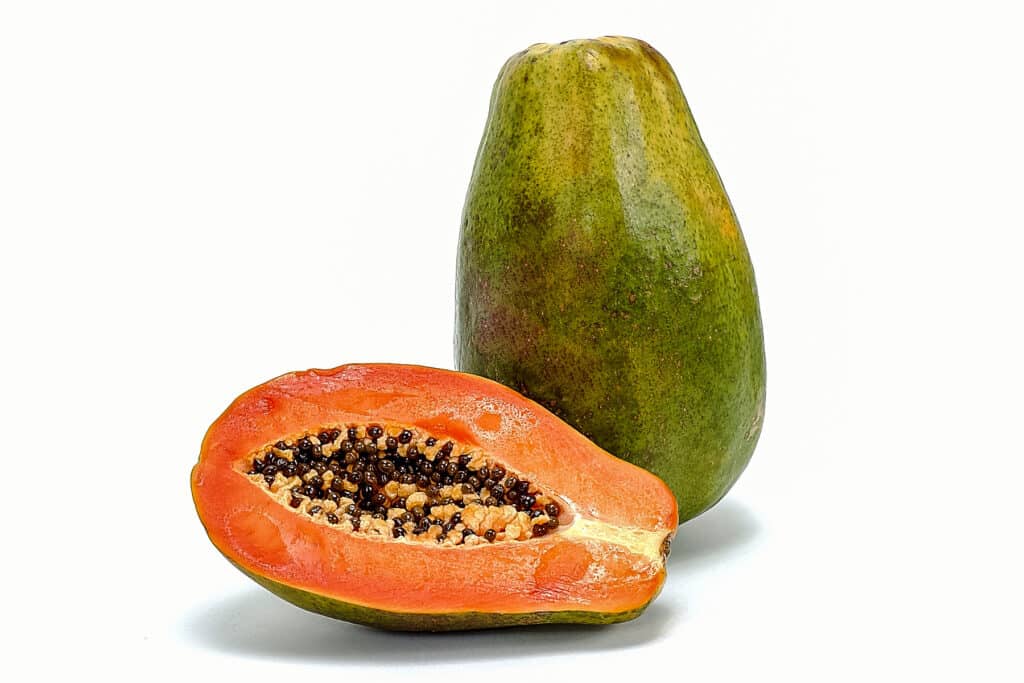 One whole Hawaiian Sunrise Papaya with half of one next to it showing the flesh and seeds.