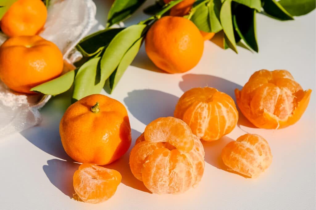 Several tangerines and their green leaves with a few peeled.