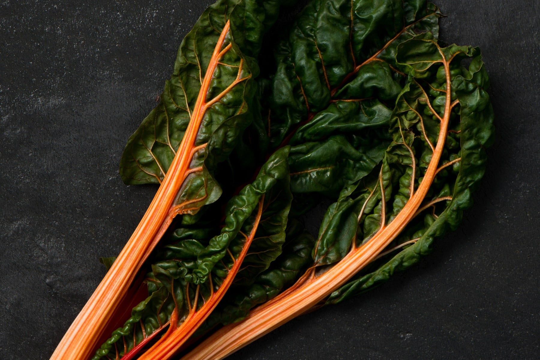Three stalks of orange swiss chard on a black surface.