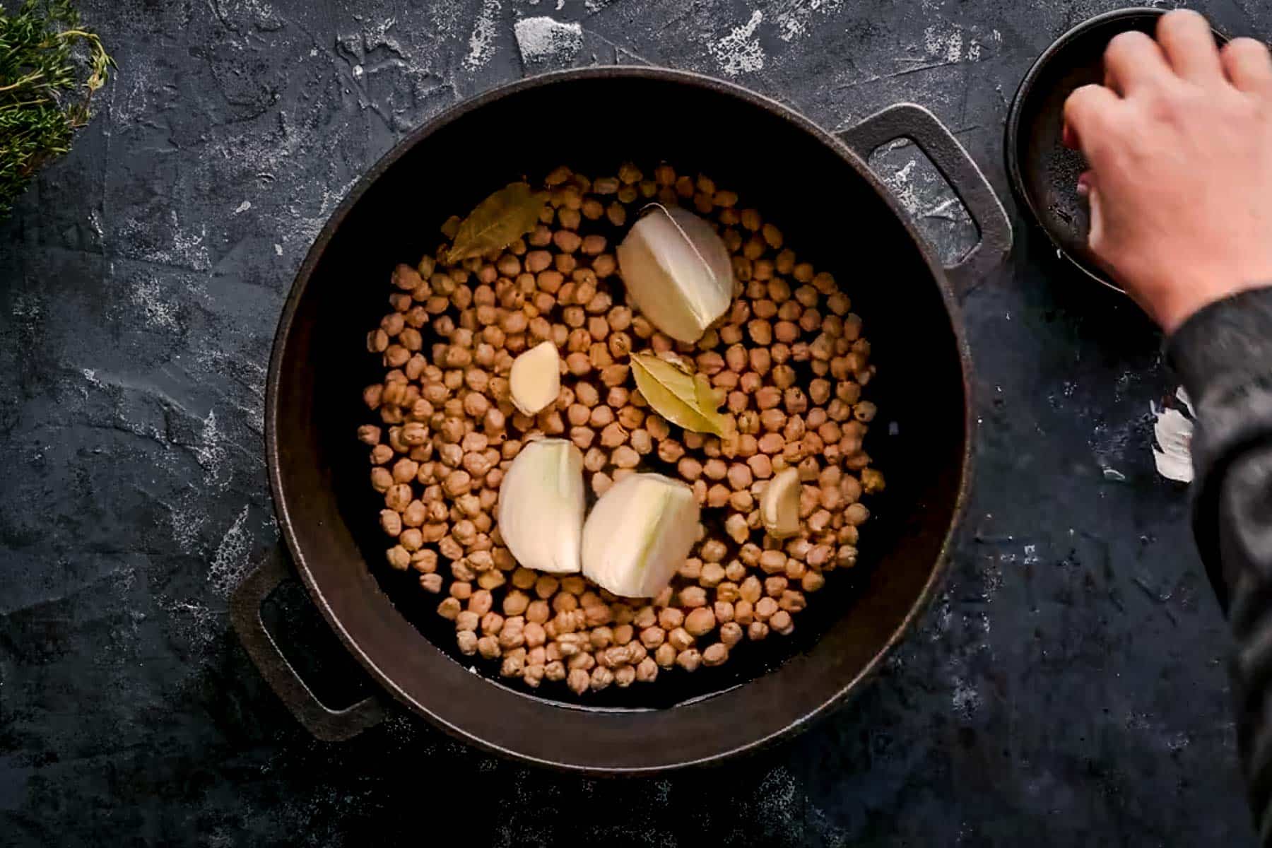 Dried garbanzo beans in a cast iron pot with aromatics including onion and garlic.