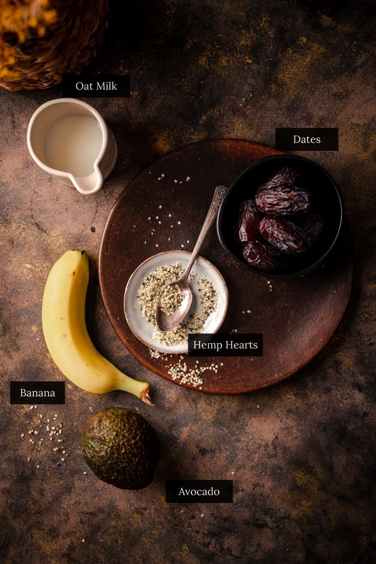 A dark background featuring an avocado banana smoothie with a small pitcher of oat milk.