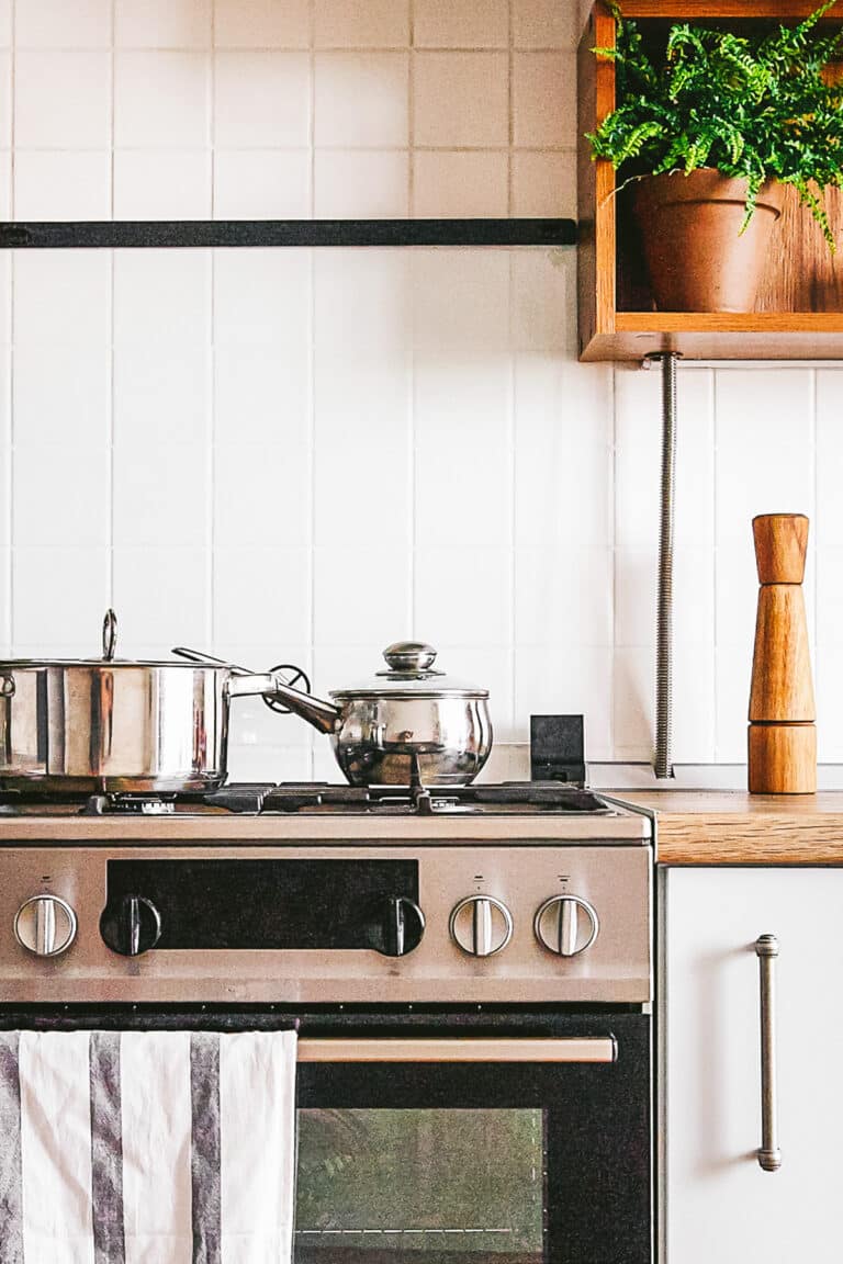 White kitchen with stainless steel range and stainless steel pots on top.