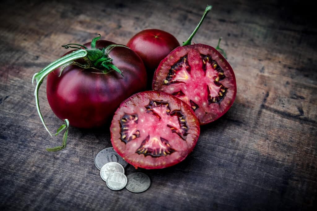Three tula black tomatoes with one cut in half. They are pink-red to black in color.