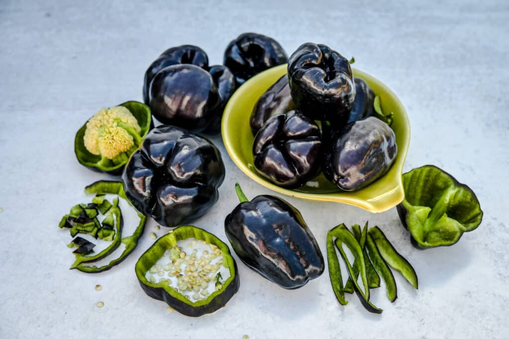 Black zulu peppers in a lime green bowl. Some cut in half showing their lime green flesh.