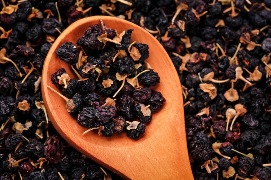 Dried Black Goji Berries with a wooden spoon picking some up.