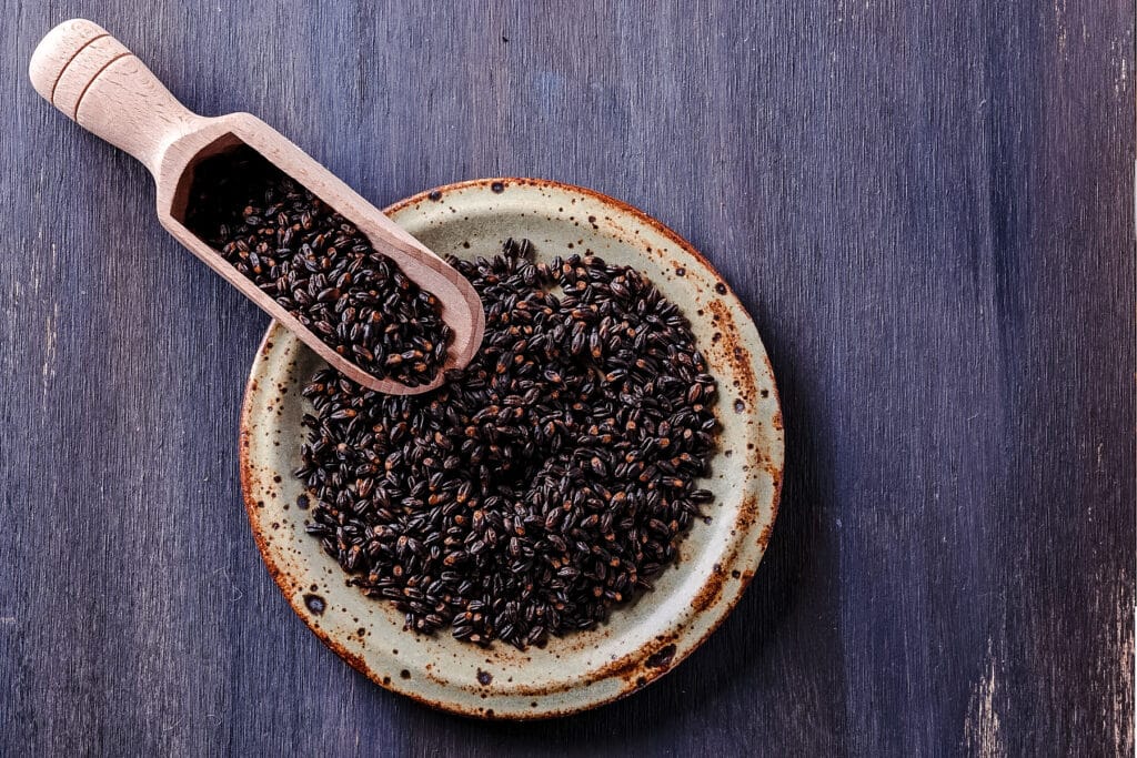 Small bowl of black barley with a wooden scoop filled next to it.