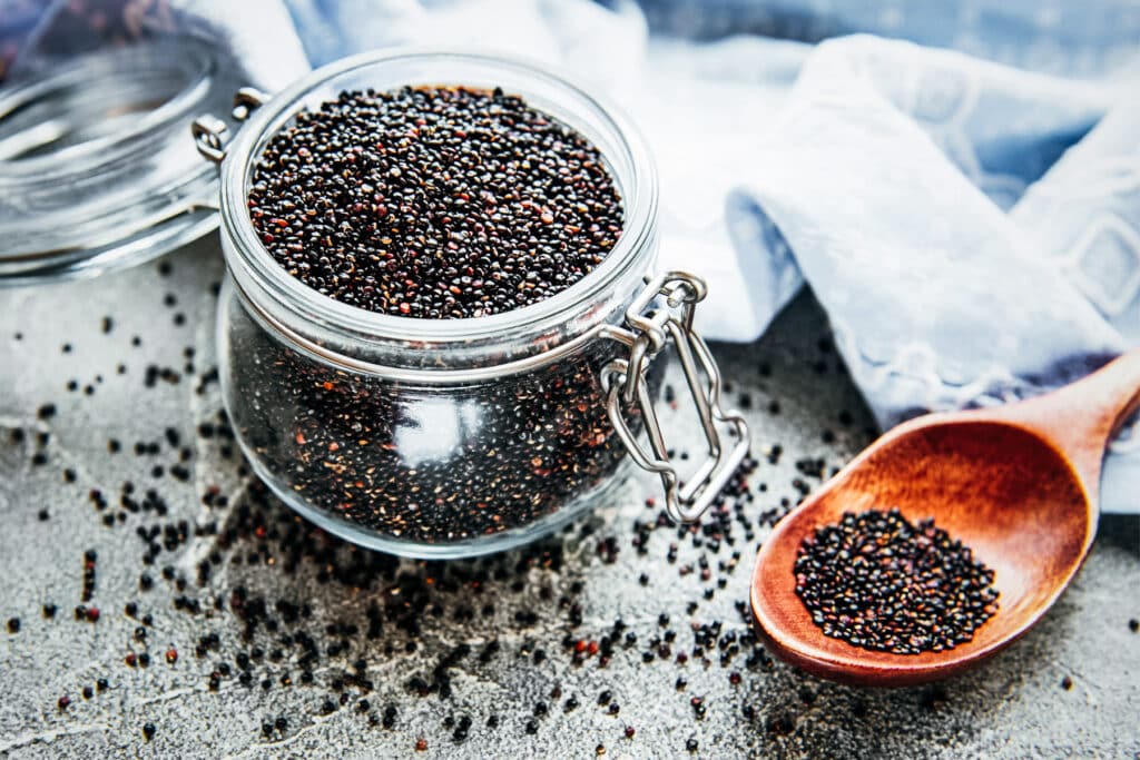 Glass jar of black quinoa with a wooden spoon next to it and a light blue napkin.