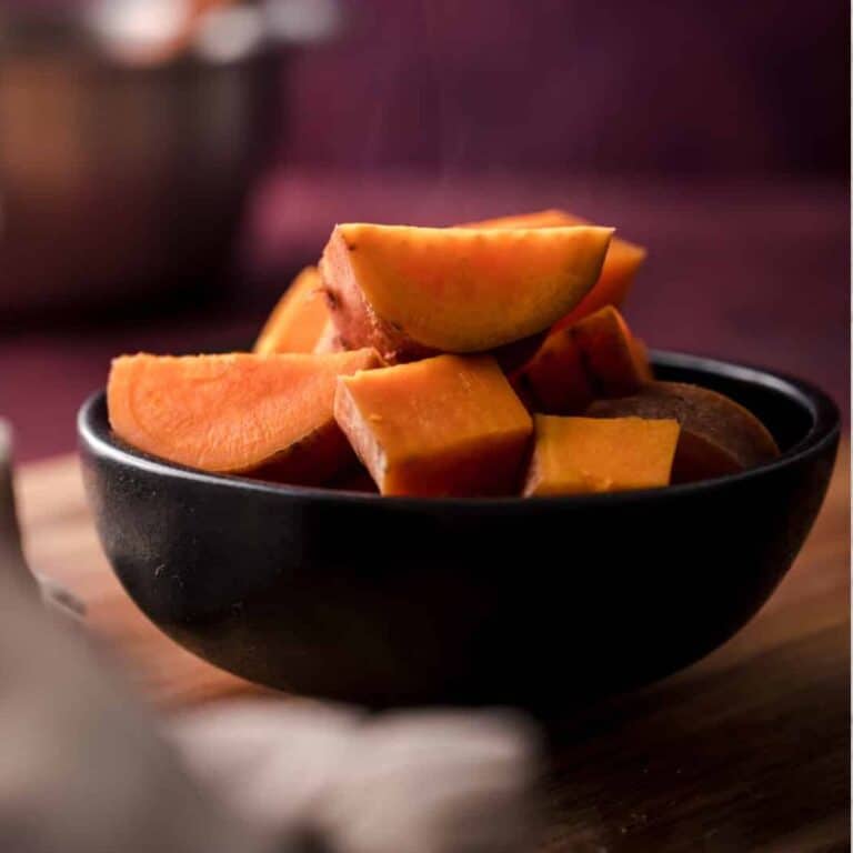 A black bowl filled with sliced pieces of cooked sweet potato on a wooden surface, showcasing the delicious results of learning how to boil sweet potatoes.