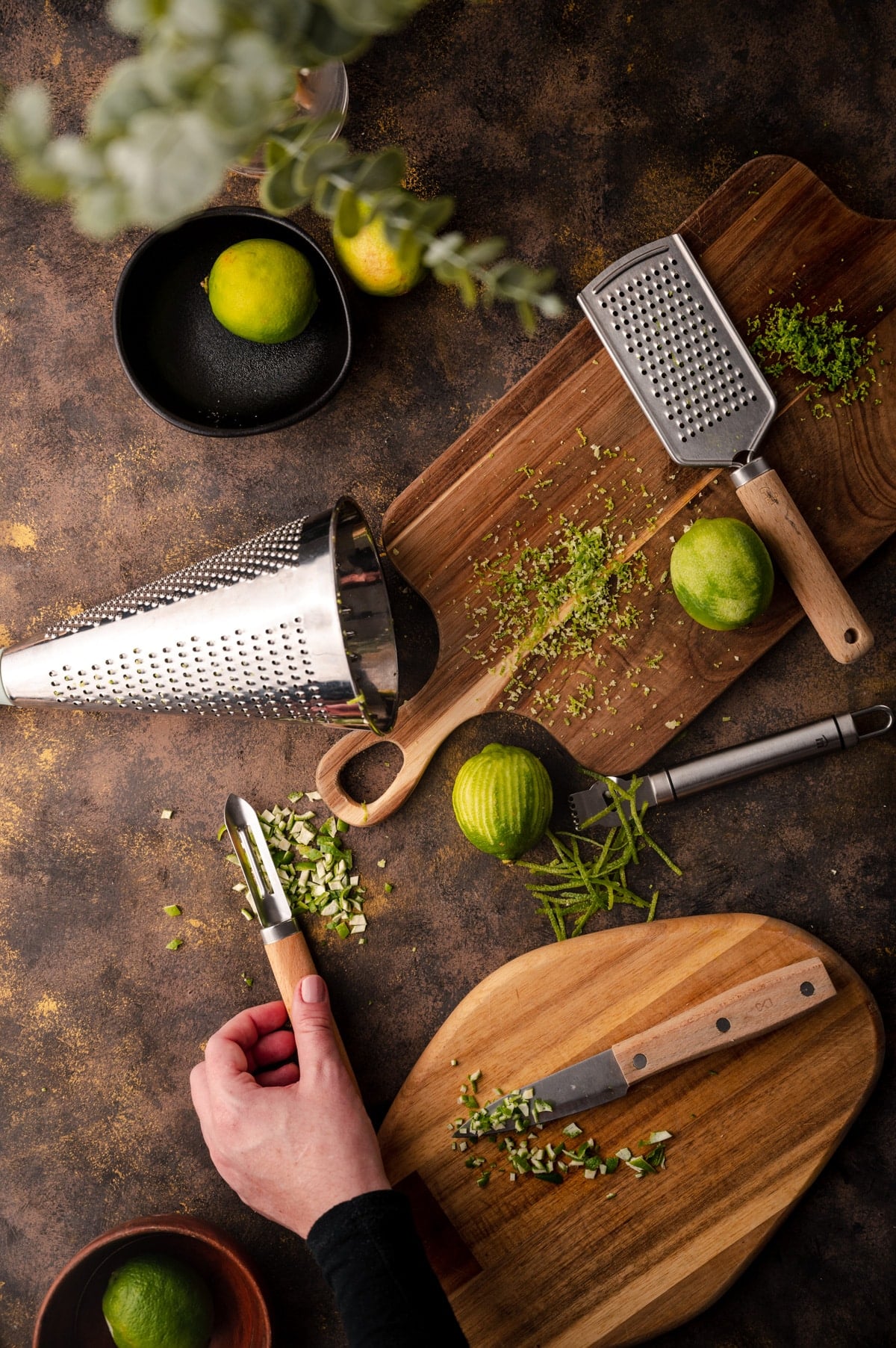 Wooden cutting boards and citrus zesters with a woman's hand picking up a veggie peeler.