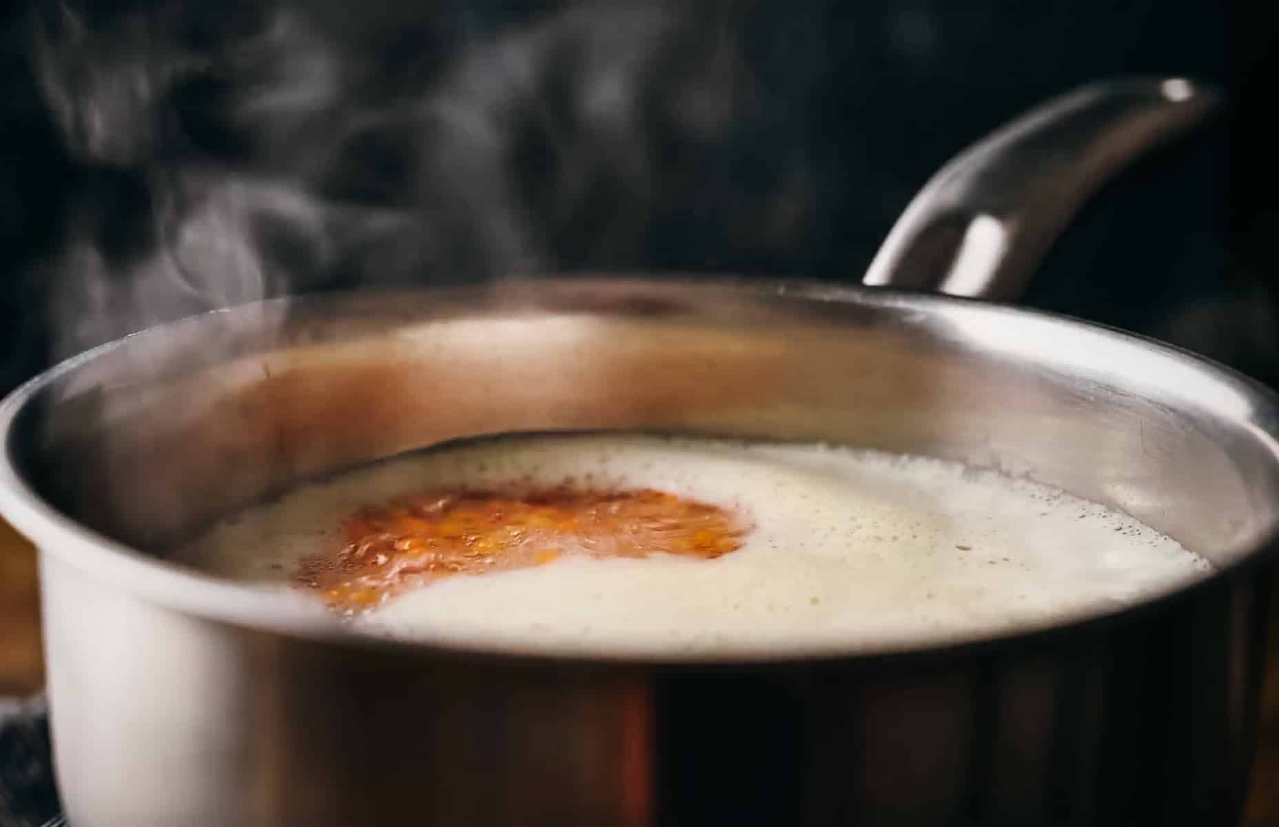 A close-up of a stainless steel pot on a stove containing boiling lentils and water.