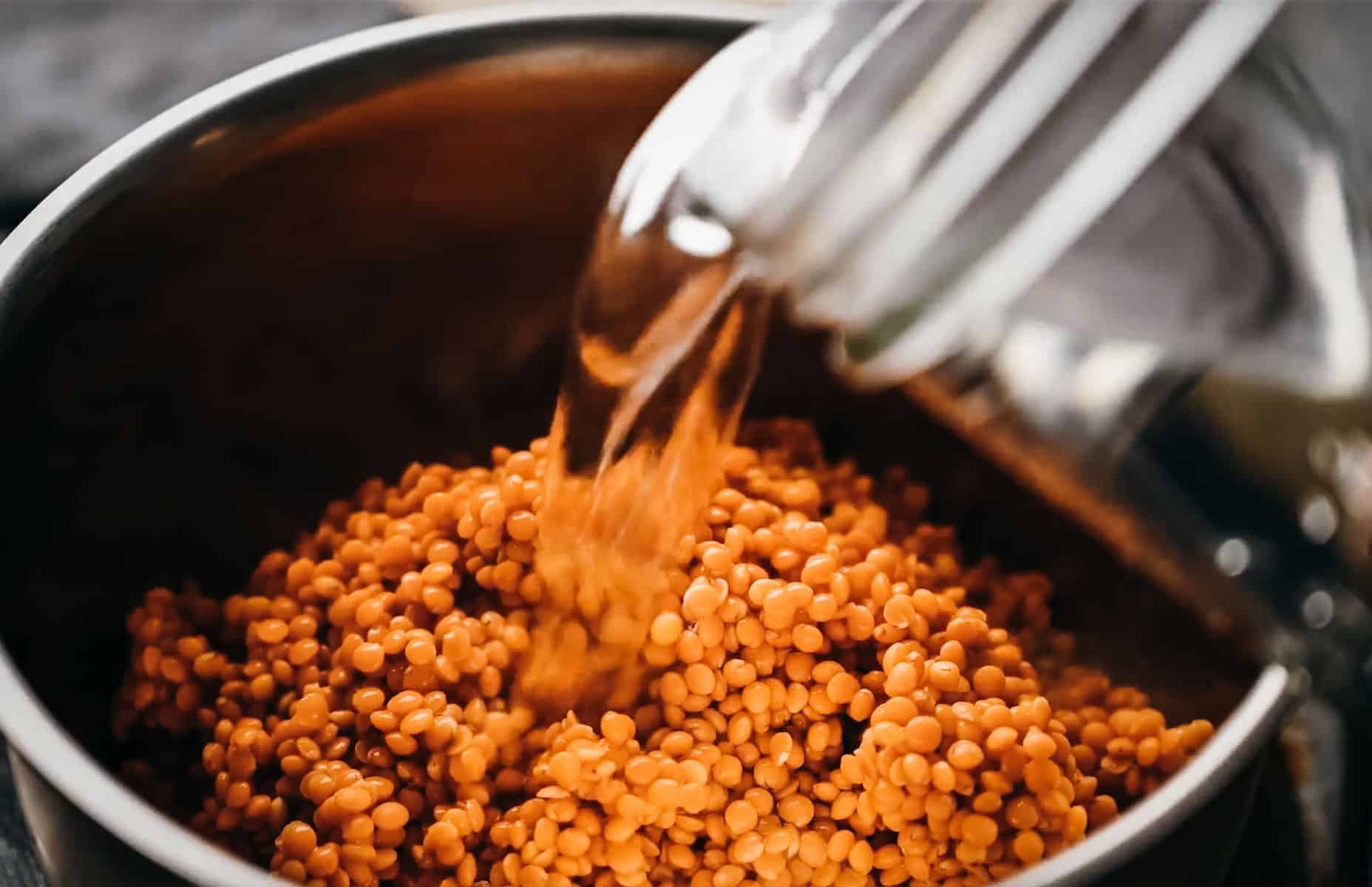 Water is being poured into a pot containing red lentils.