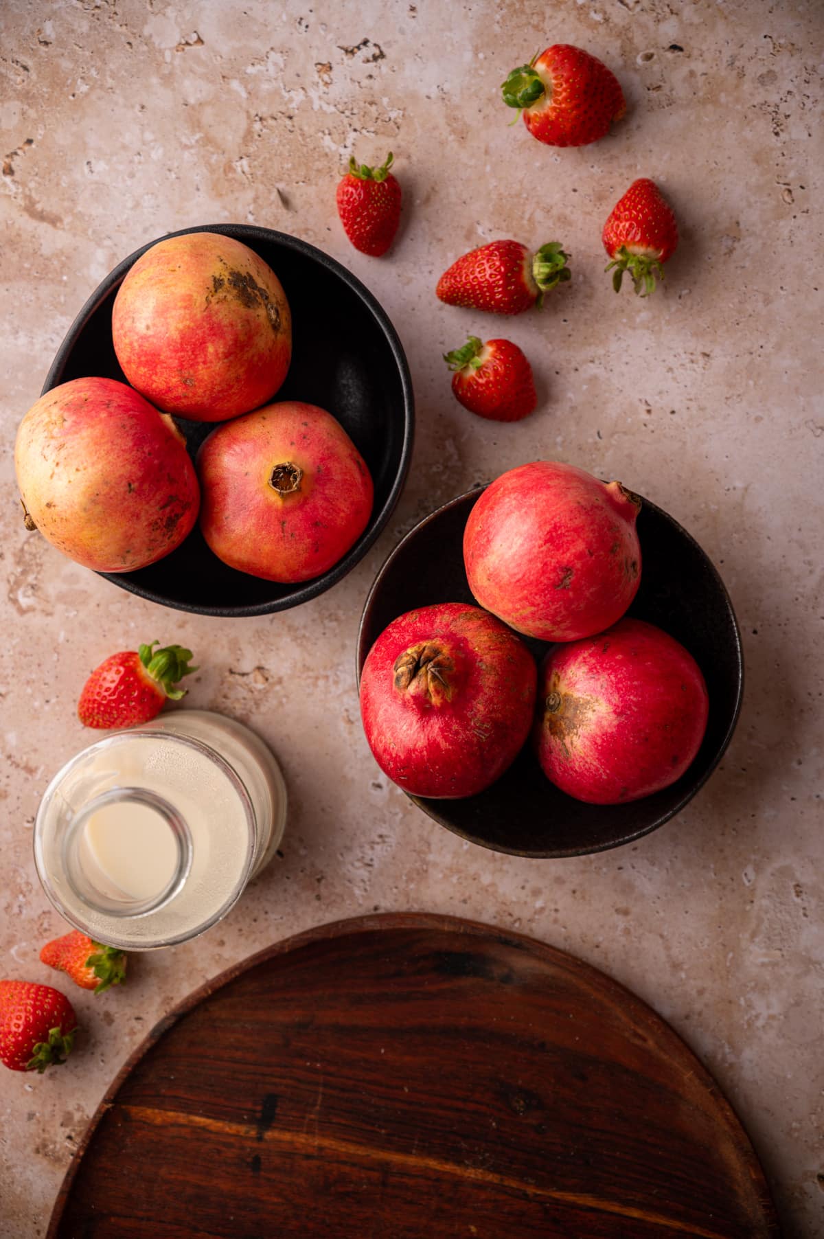 Pomegranates in black bowls, with strawberries and nut milk.