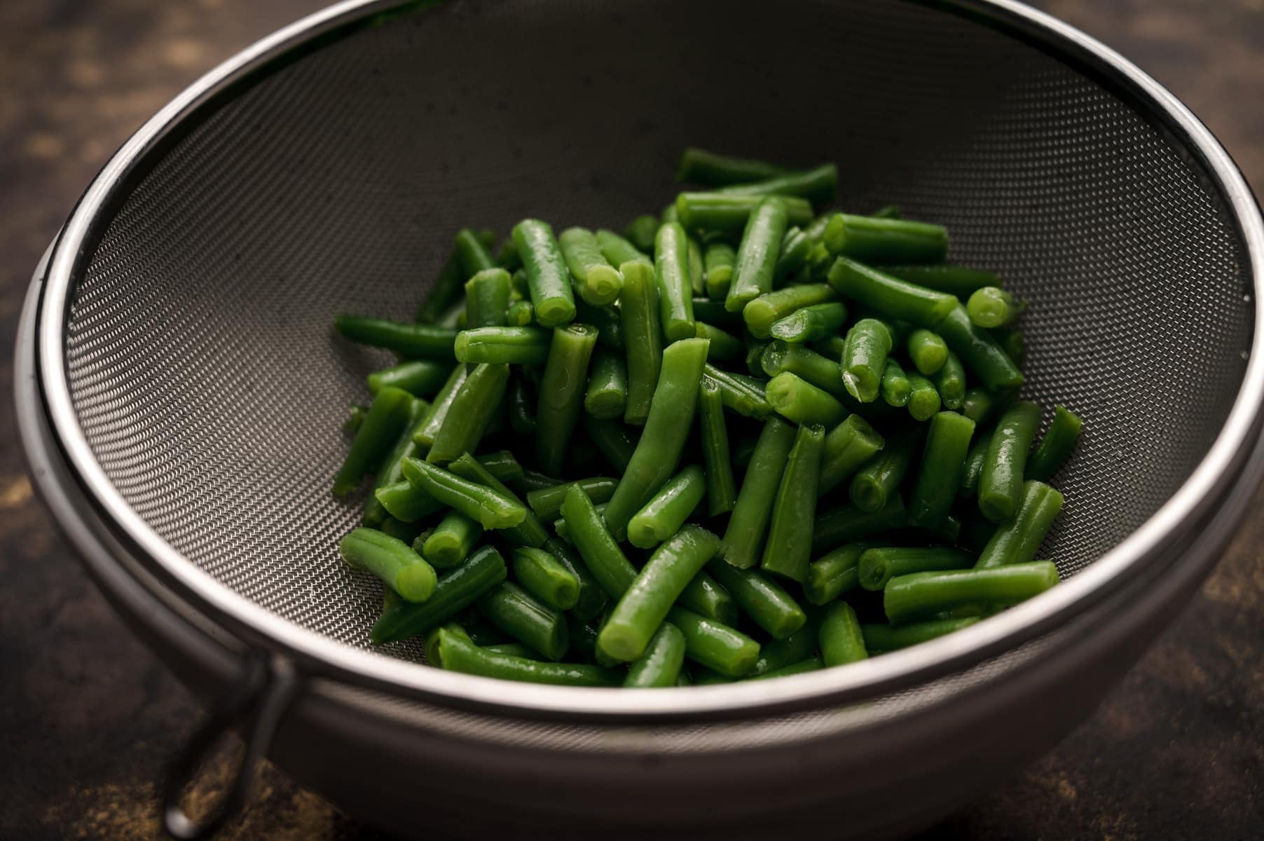 Canned green beans in a metal mesh strainer getting drained.