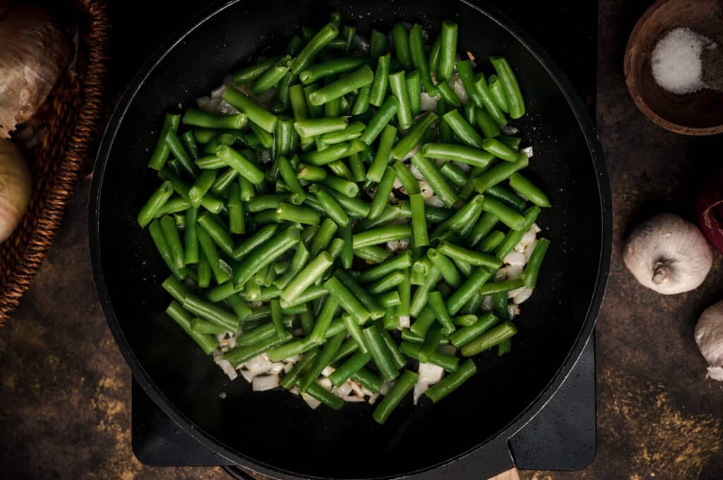 Cooking green beans on the stovetop with onion, garlic, and spices.