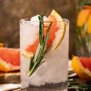 A glass filled with ice, grapefruit water, a grapefruit slice, and a sprig of rosemary.