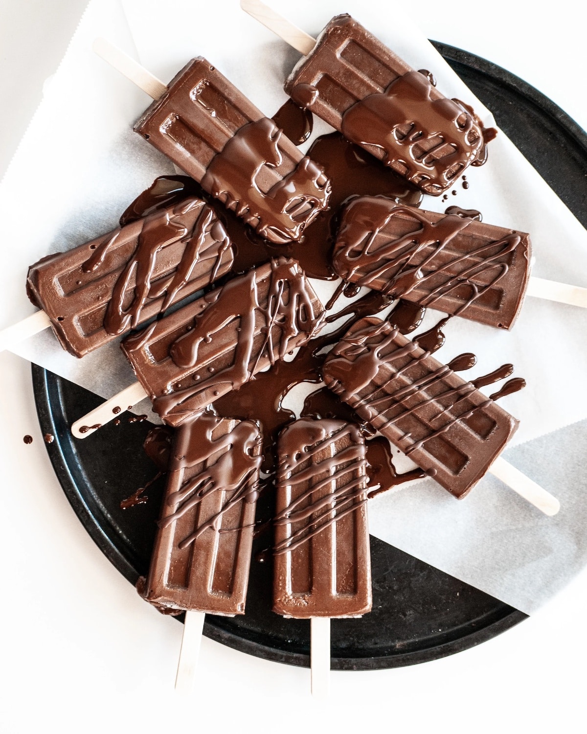 Eight vegan fudge pops on a black plate drizzled in chocolate.