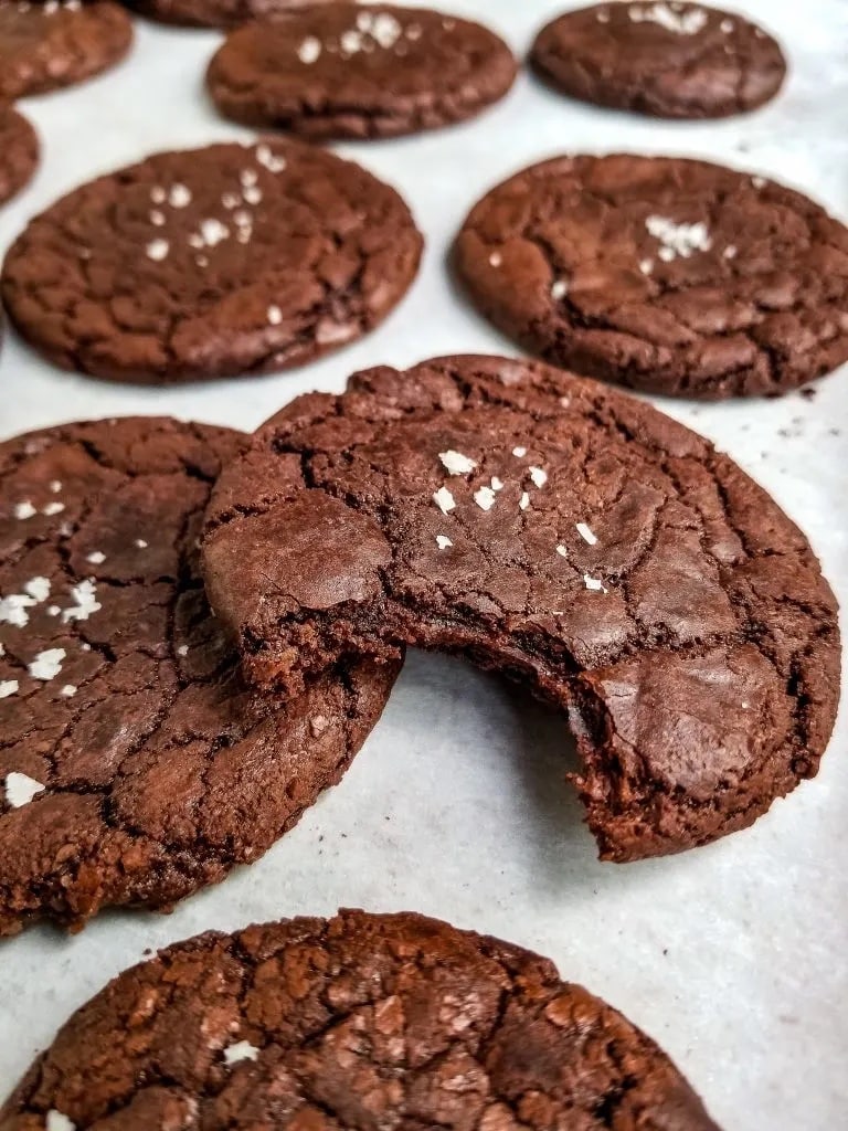 Large chocolate crackle cookies with a bite taken out.