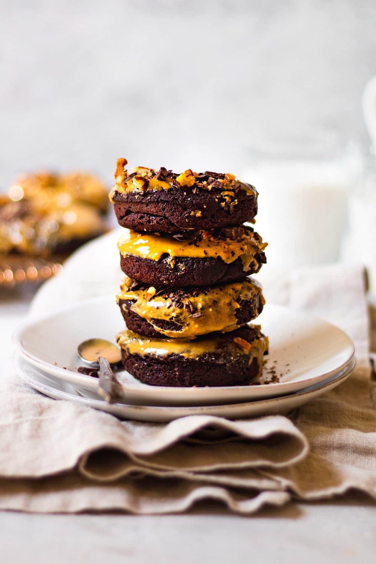Four chocolate donuts with peanut butter glaze stacked on top of each other on a white plate.