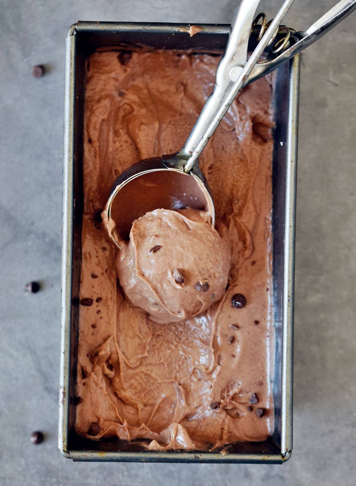 Metal loaf pan filled with vegan chocolate ice cream and an ice cream scoop scooping some out.