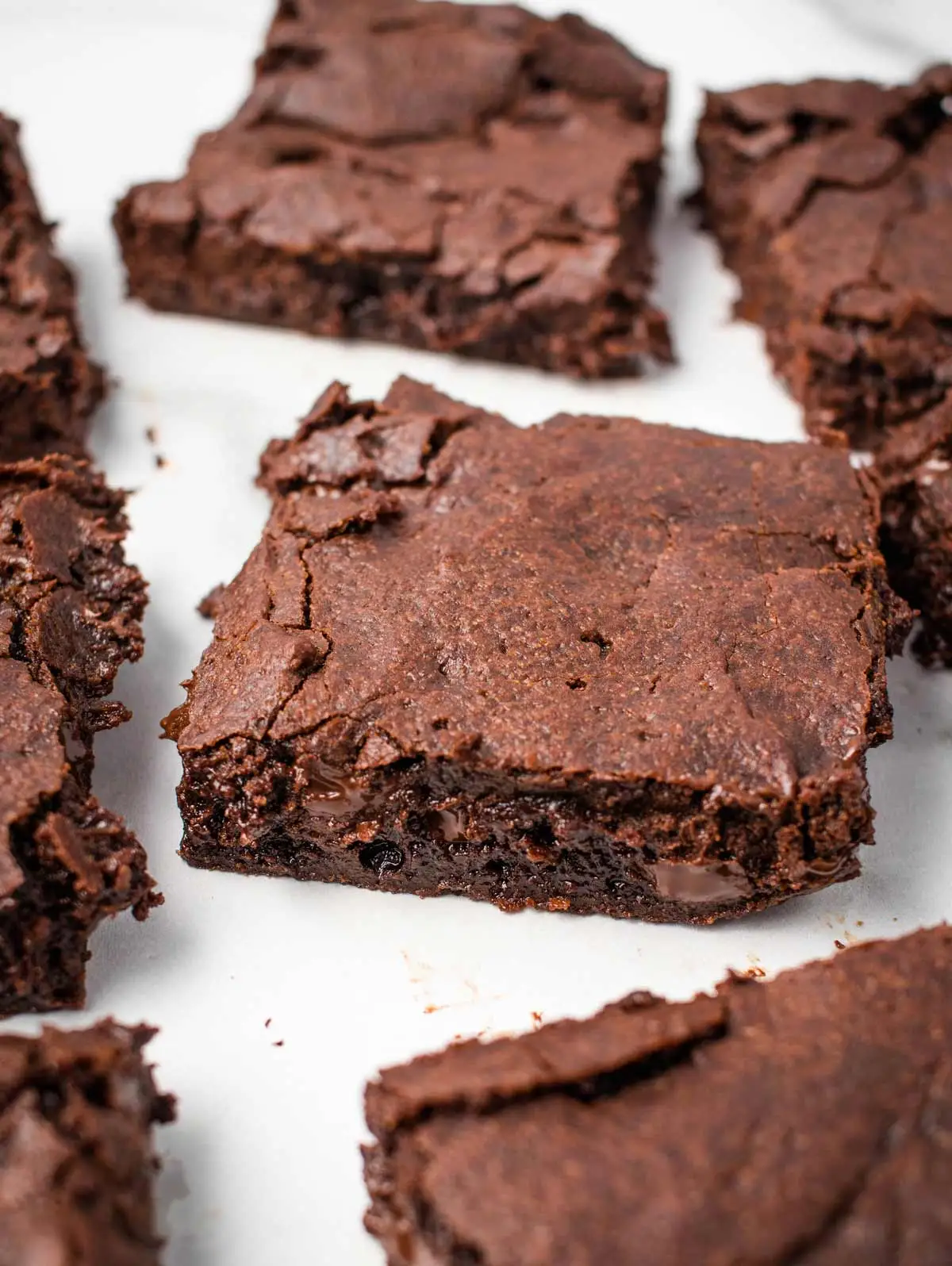 Several square brownie slices spread out on a white surface.