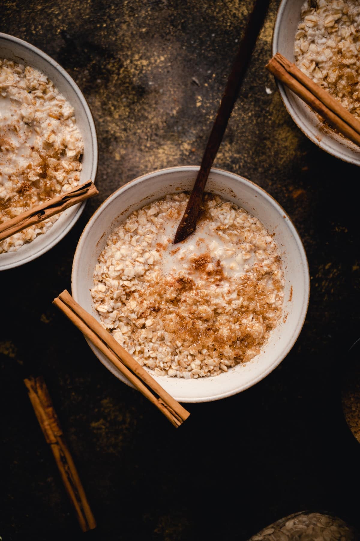 A bowl of oatmeal topped with milk, cinnamon sticks, and ground cinnamon.