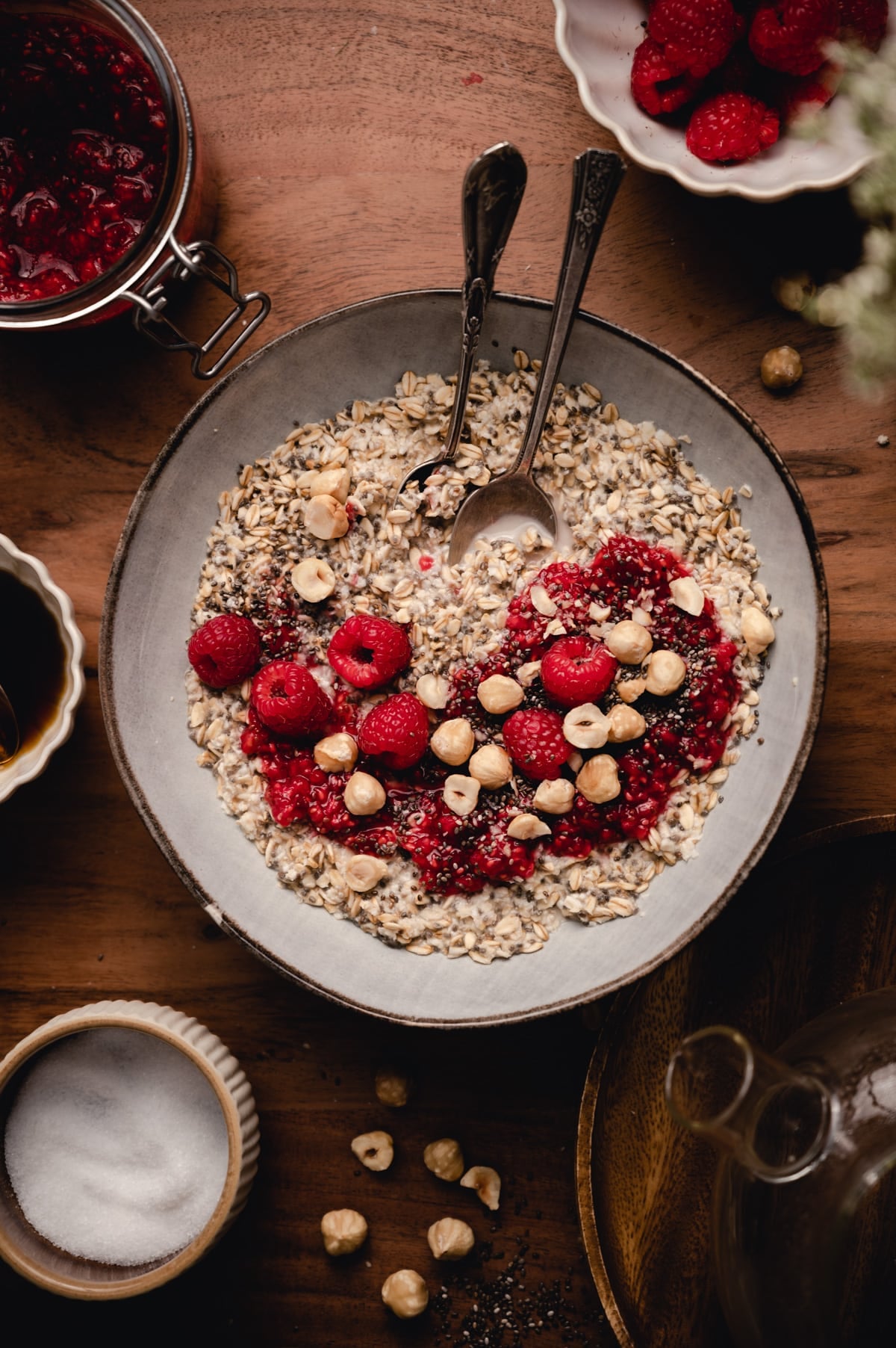 Top down photo of chia oats with fresh raspberries hazel nuts on top surrounded by ingredients.