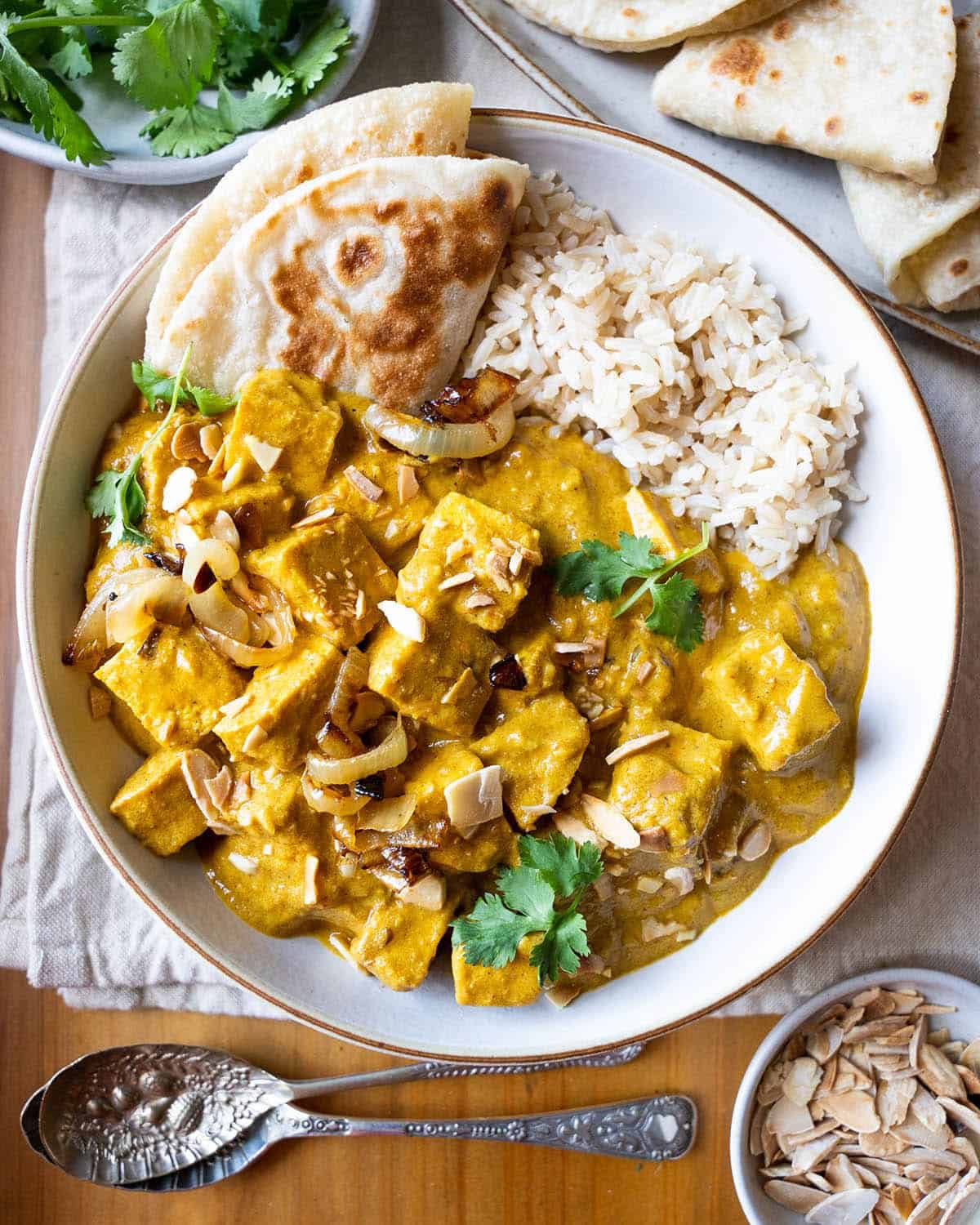 A bowl of vegan tofu curry with rice and naan.