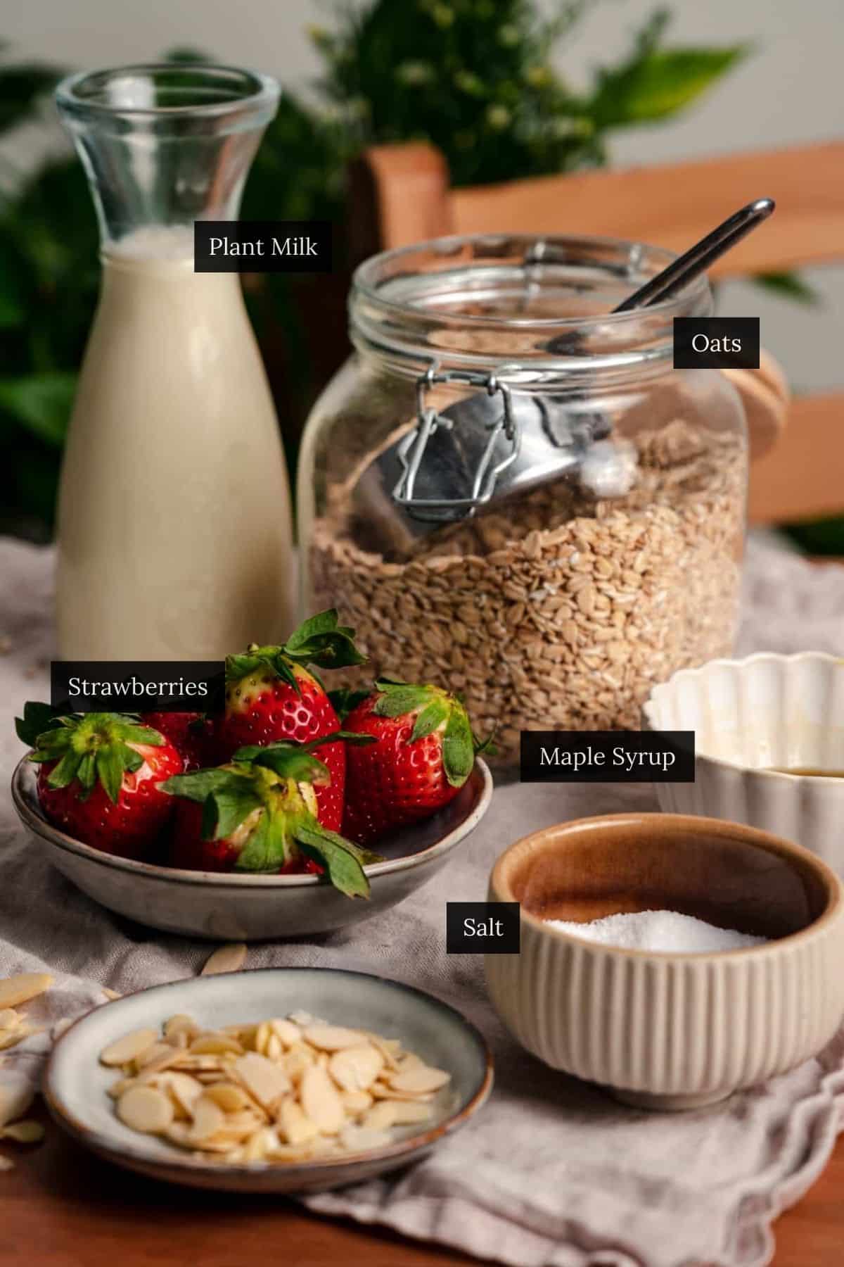 Ingredients for strawberry oatmeal set on a table with them labeled.