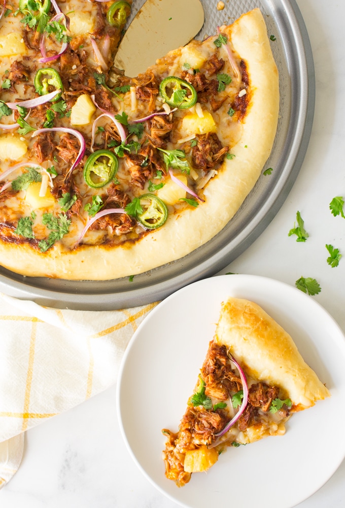 The pizza features pulled jackfruit, pineapple, red onion, jalapeños, and cilantro on a tray.